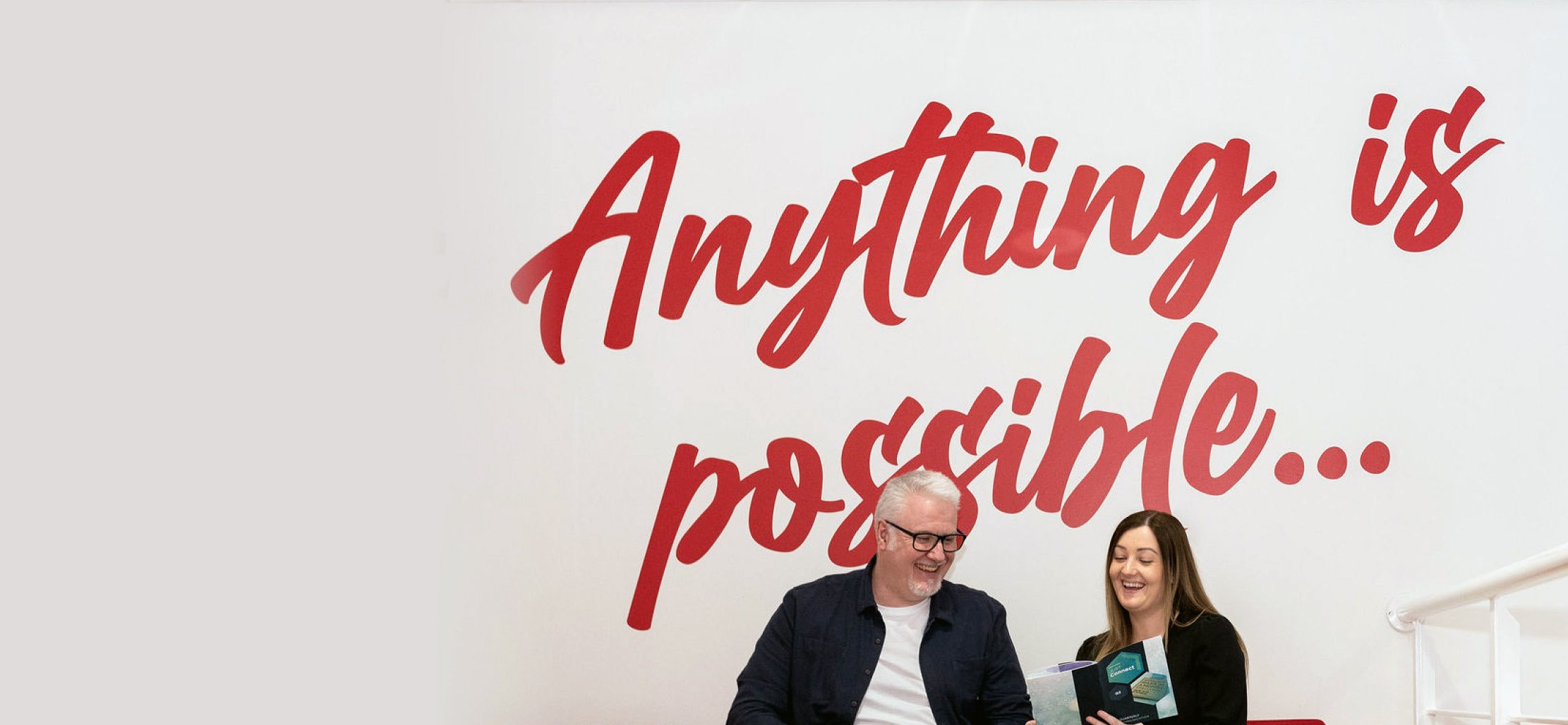 Graphic Services team members reviewing a funeral stationery brochure beneath a wall message reading 'Anything is possible'