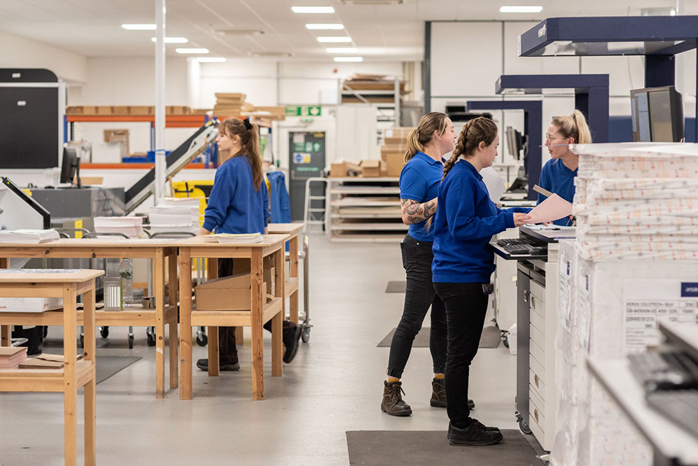 Print operators running digital presses to produce high quality funeral stationery in a production hall